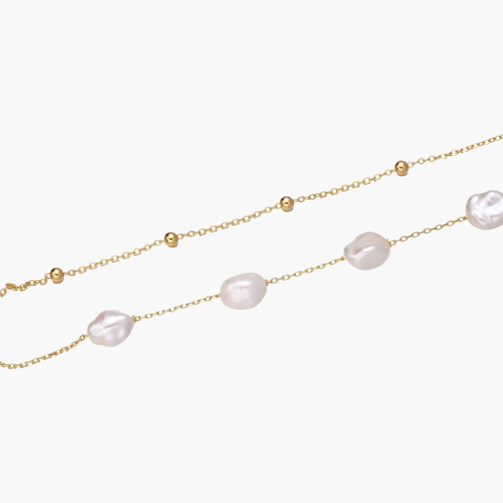 Double-strand gold bracelet with irregular baroque pearls and smooth freshwater pearls on cream background.