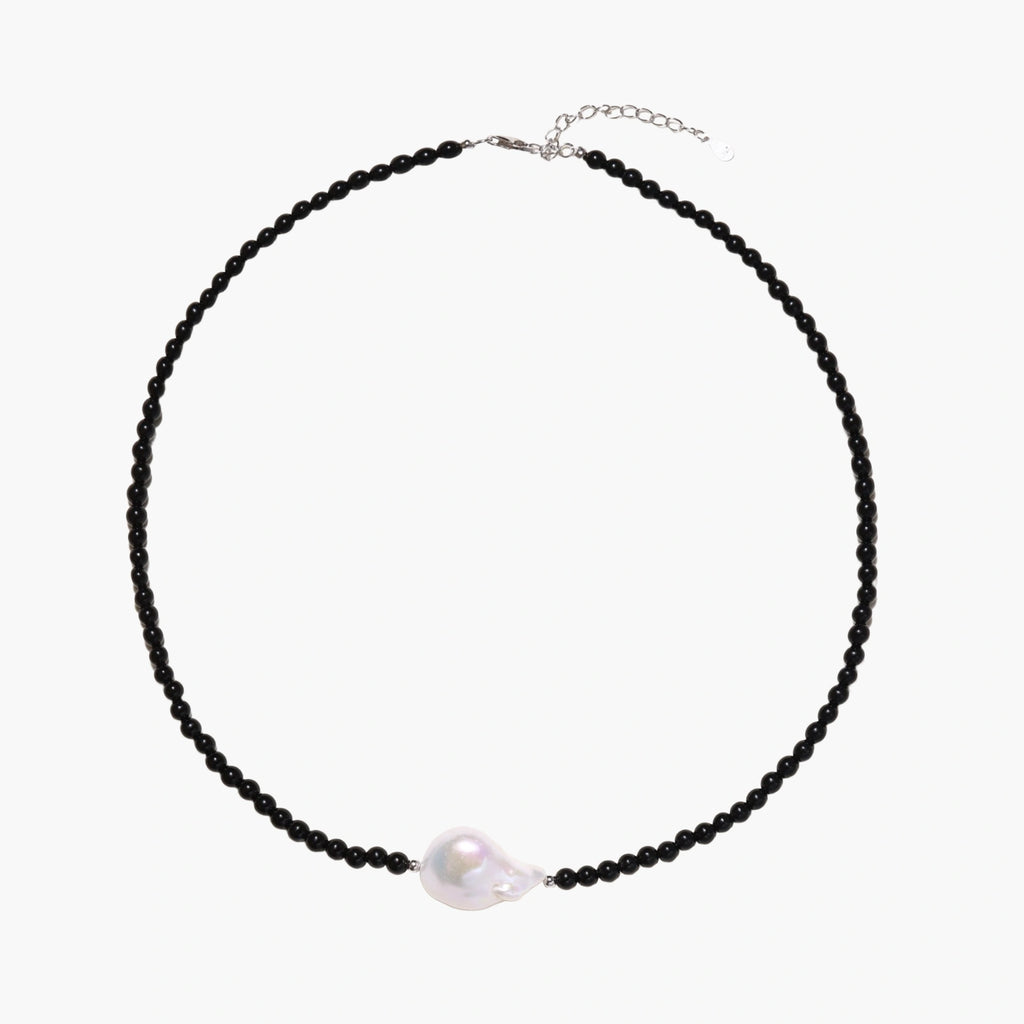 Beaded black agate necklace with iridescent baroque freshwater pearl centerpiece on cream background.