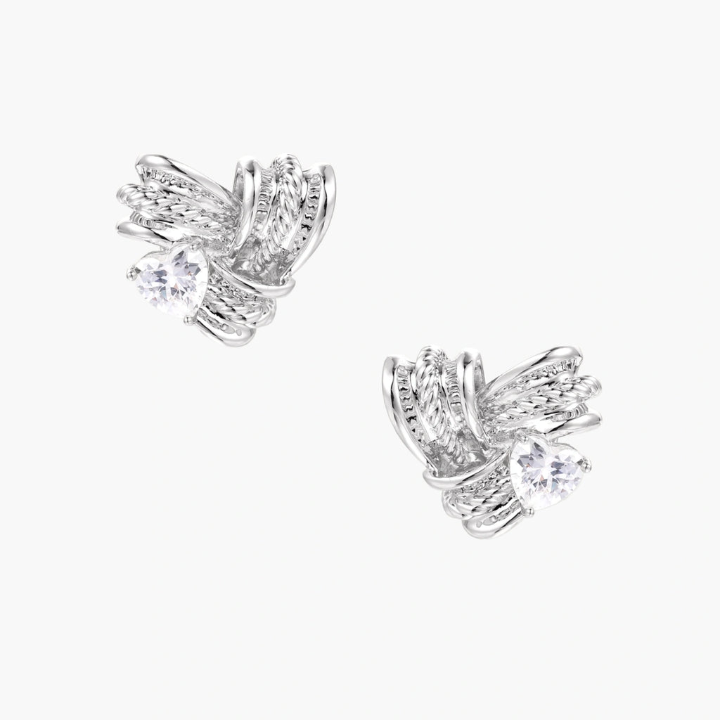 Pair of sculptural white gold-plated stud earrings with twisted ribbon design and sparkling zirconia stones on cream background