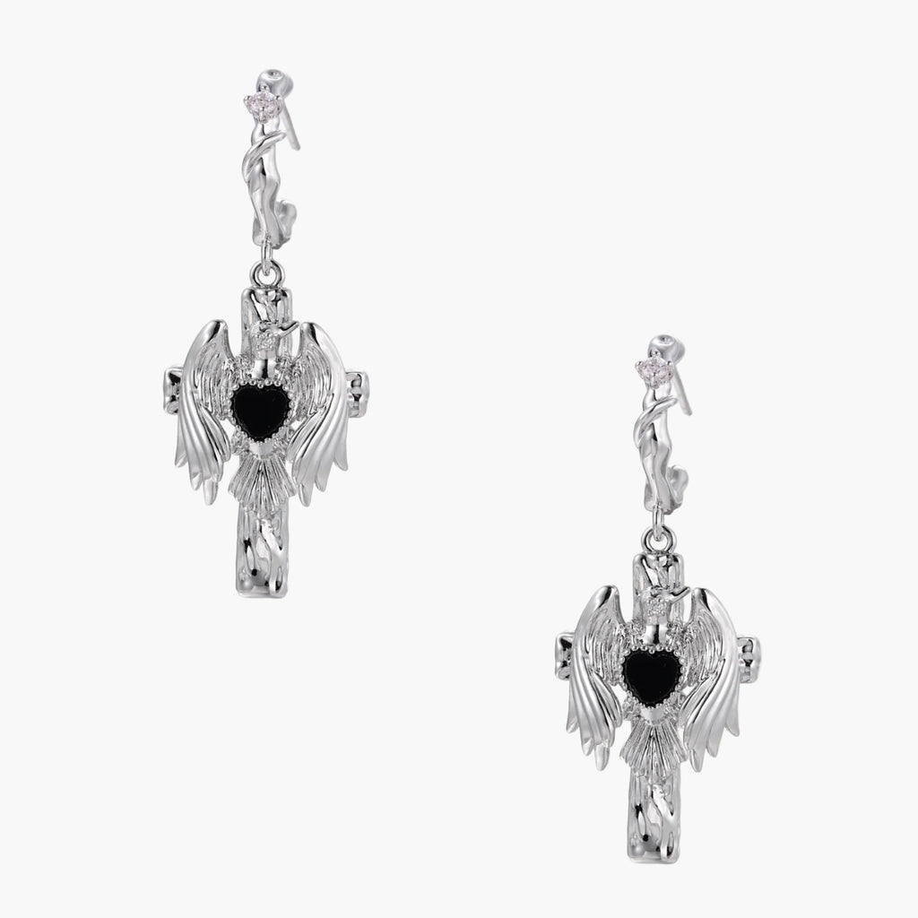 Silver drop earrings with twisted hoops and angel wings embracing black heart locket on white background.