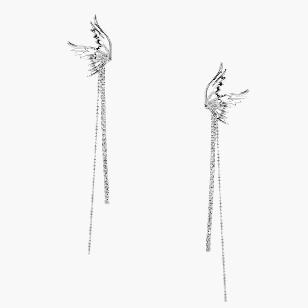 Pair of silver wing-shaped earrings with feather details and long sparkling crystal chain drops on cream background