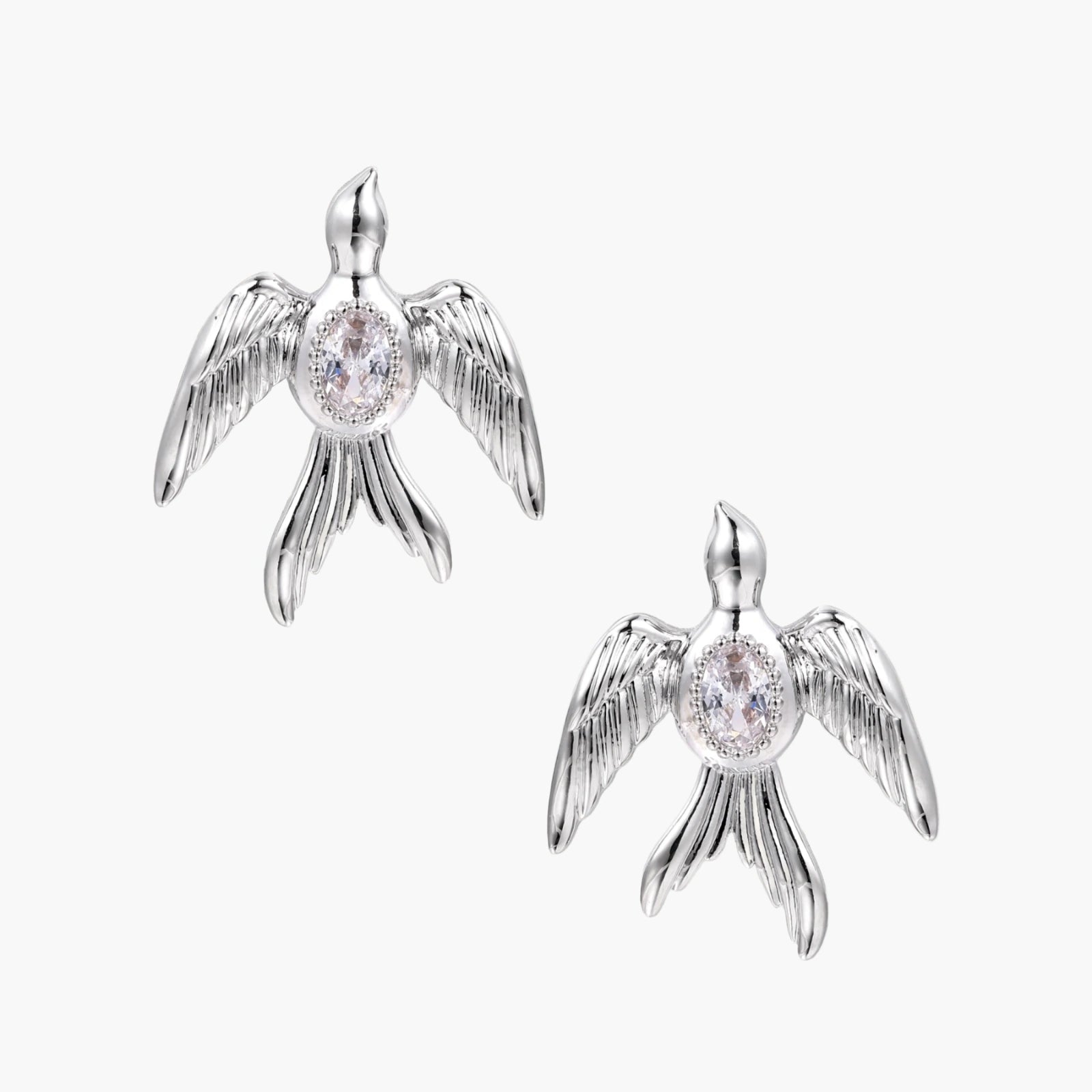 White gold-plated bird earrings with spread wings and oval zirconia center on cream background