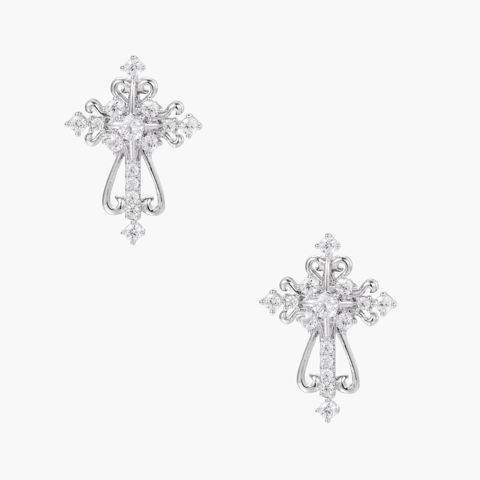 White gold-plated baroque cross studs with zirconia stones and ornate scrollwork on cream background.
