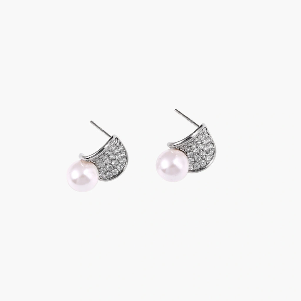 Curved pavé diamond studs in white gold-plated brass cradle lustrous freshwater pearls against cream background