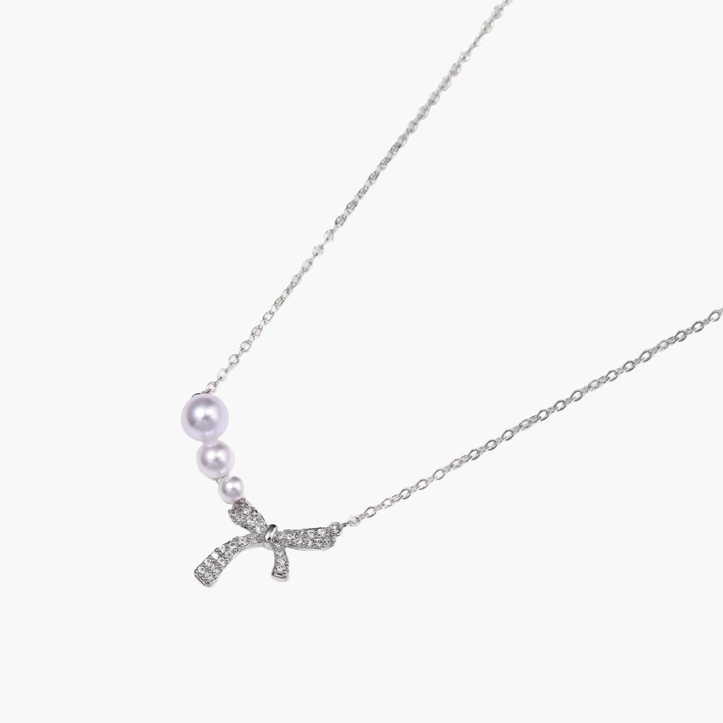 Delicate white gold plated necklace with freshwater pearls and sparkly crystal bow pendant on white background