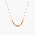 Delicate gold-plated necklace with graduated spherical beads forming gentle smile curve on beige background
