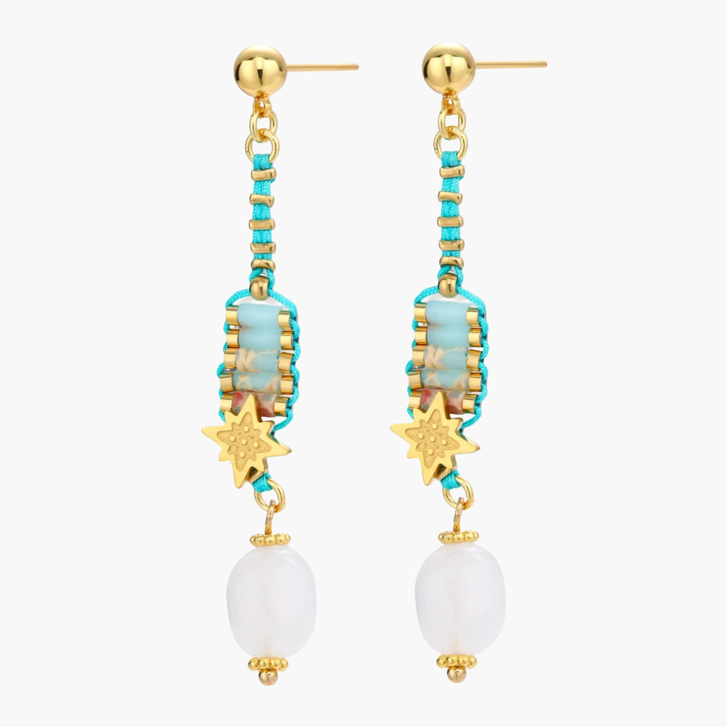 Gold-plated dangle earrings with turquoise threading, star charms, and white pearl beads against cream background.