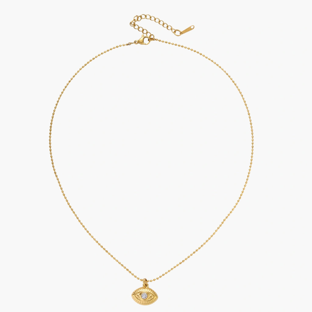 Layered necklace with green stone beads, gold spacers, white accents, and protective eye pendant on cream background.