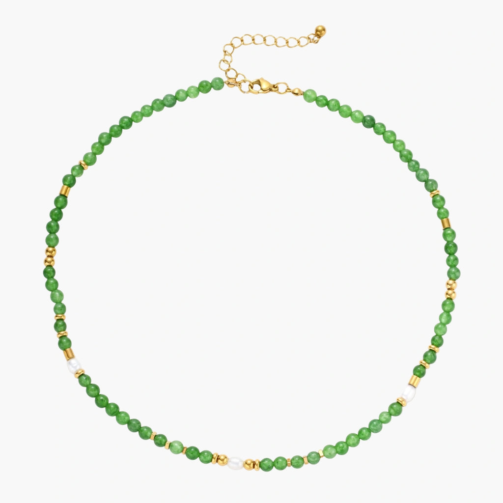 Layered necklace with green stone beads, gold spacers, white accents, and protective eye pendant on cream background.